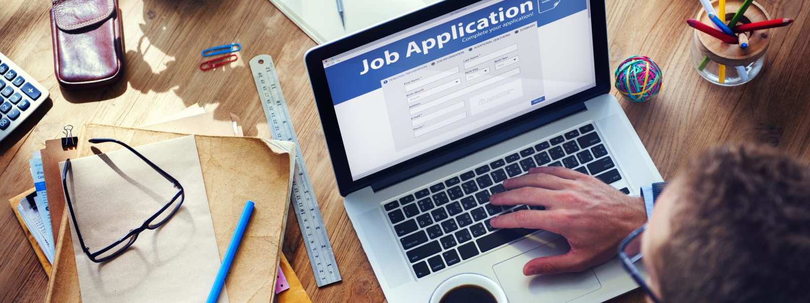 job application on laptop at a desk with glasses and pens