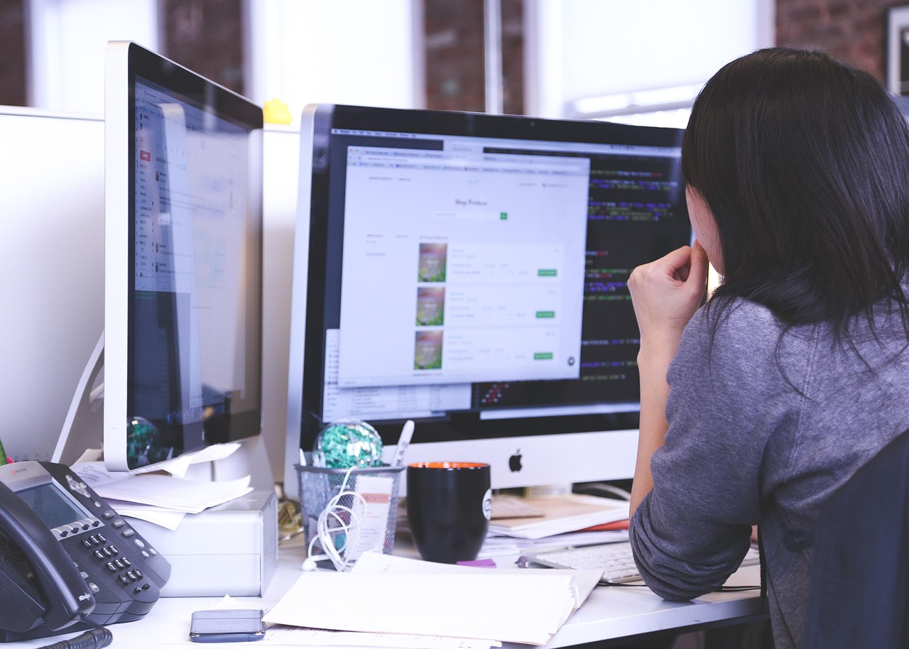 a woman looks at two large desktop computers